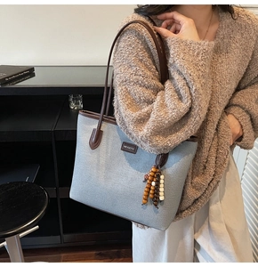 Close-up of light grey tote bag with brown leather trim and retro beaded charm accessory