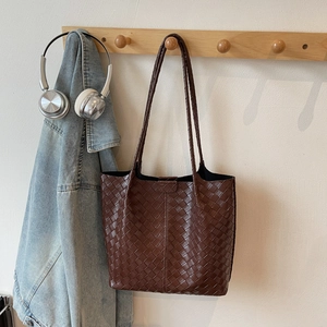 Detailed close-up of dark brown woven leather tote bag with cross-stitch craft on wood hook