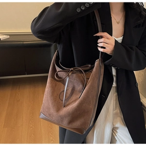 Detail of a large brown suede bucket tote bag with leather straps and bow tie accent