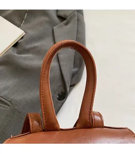 Detail of the brown leather backpack handle with reinforced stitching and soft texture