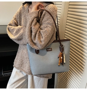 Close-up of grey-blue tote bag featuring wood bead tassel and leather handles
