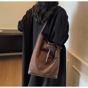 Detail of dark brown matte suede bucket bag with a decorative bow and leather reinforced base