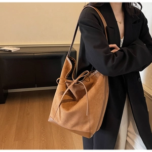Detailed view of brown suede bucket tote bag with delicate leather bow on female model