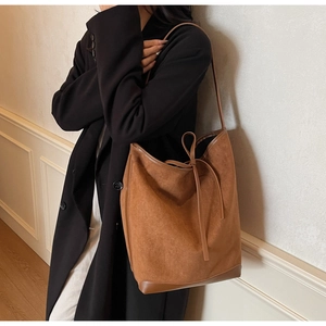 Side view of a large brown suede tote bag carried by a model in a black winter coat