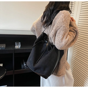 Detail view of black bucket bag featuring leather trim and elegant bow closure design