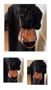 Detail of brown leather bucket bag featuring gold chain and ethnic beaded tassel charm