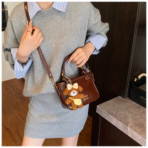 Détail d'un mini sac seau marron foncé avec finition brillante et charm ours en peluche