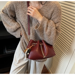 Detail of burgundy drawstring bucket bag with retro wooden bead pendant and chain
