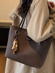 Brown canvas tote bag with leather trim and beaded tassel accessory on beige coat