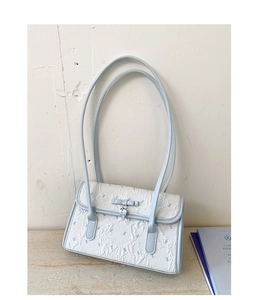 Detail of light blue bow and silver heart pendant on a white pleated shoulder bag