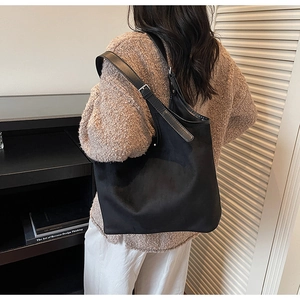 Detail view of a large black velvet tote bag with an adjustable strap on a female model