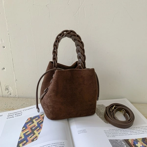 Close-up of brown suede bucket bag with woven handle and detachable shoulder strap
