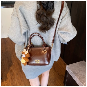 Détail d'un sac seau marron avec charm ours peluche et logo doré sur cuir brillant