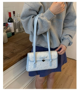 Detail of light blue underarm bag featuring a ribbon bow and heart-shaped pendant detail