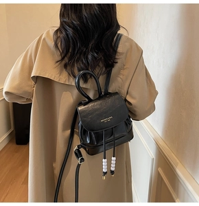 Detail of black faux leather backpack featuring golden logo and white beaded drawstring