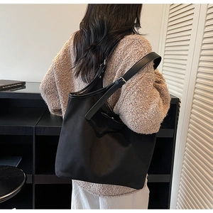 Detail of black tote bag with adjustable leather strap worn by model in minimalist setting