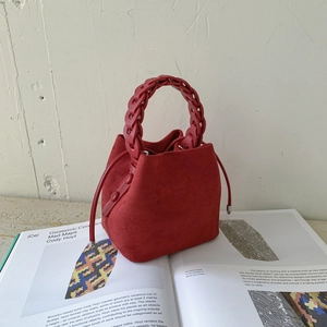 Detail of red suede bucket bag with woven handle and drawstring on an art book