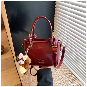 Détail du sac seau bordeaux en similicuir avec logo métallique et porte-clés ours