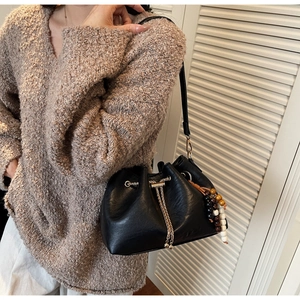 Detail of black leather bucket bag with chain closure and bead charm on model