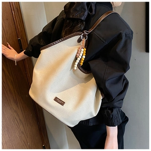 Detail of canvas tote bag featuring brown leather trim and colorful bohemian bead tassel