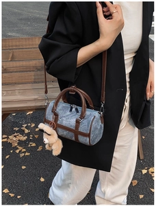 Bolso cilíndrico de mezclilla azul con asas de cuero marrón y dije de oso en exterior