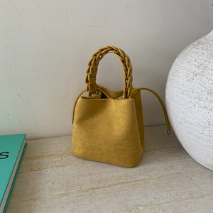 Detail of yellow suede bucket bag featuring a decorative woven handle on marble surface