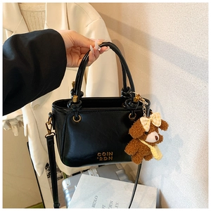 Détail d'un sac seau en cuir noir avec texte doré 'COIN 2DH' et breloque ours marron mignonne