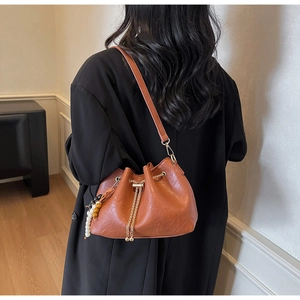 Close-up of caramel leather bucket bag with gold chain drawstring and beaded tassel detail