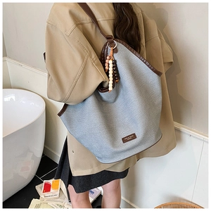 Detailed side view of grey fabric tote bag with brown leather trim and beaded charm