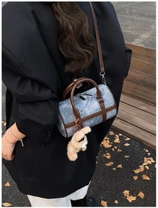 Detalle del bolso cilíndrico de mezclilla azul con asas de cuero marrón y oso de peluche