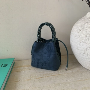Detailed close-up of dark blue suede bucket bag featuring thick braided handle and drawstrings