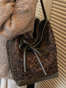 Leopard print large tote bag with dark green leather trim worn by a model in autumn