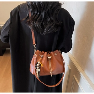 Detail of brown leather bucket bag with gold chain and colorful beaded charm on side
