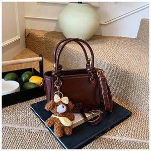 Détail d'un sac seau en cuir marron foncé avec un charm ours en peluche sur une pile de livres