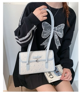 Detail of cream pleated shoulder bag with blue bow accent and metal heart pendant