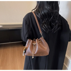 Brown bucket bag detail showing drawstring closure and decorative beaded chain on model