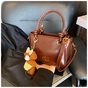 Détail d'un sac seau marron brillant avec charm ours et poignée à nœuds chic