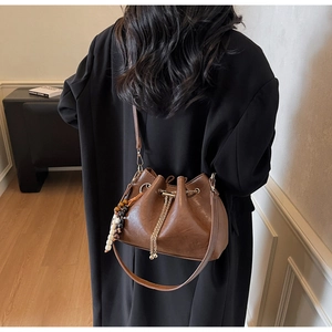 Detail shot of a brown vintage leather bucket bag with chain drawstring and beaded charm