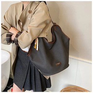 Detailed close-up of dark grey tote bag with brown leather trim and beaded pendant