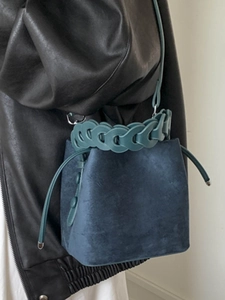 Minimalist navy blue suede bucket bag with green woven chain handle and shoulder strap