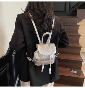 Silver metallic backpack with drawstring and pearl detail shown on a model in a suit