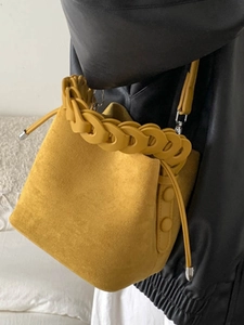 Yellow suede bucket bag featuring chunky chain handle and adjustable shoulder strap