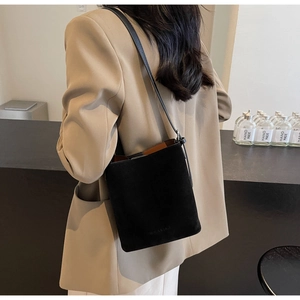 Detail view of a black suede bucket bag worn over the shoulder with a beige blazer