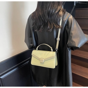 Detail view of light green commuter crossbody bag with silver buckle on black leather jacket