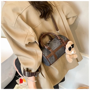 Detalle del bolso cilíndrico de mezclilla gris con asas de cuero marrón y dije de oso