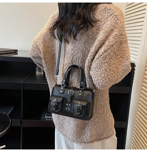 Detail of black lychee grain leather crossbody bag with silver buckles and flap pockets