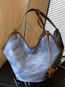 Vintage blue denim tote bag with brown leather trim and curved edge in soft lighting