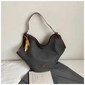 Detail of grey canvas tote bag with brown leather trim and decorative beaded charm