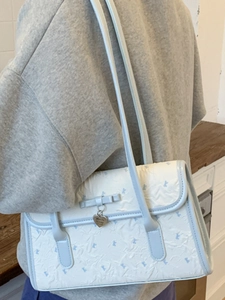 White underarm shoulder bag with blue trim and bow detail in a casual indoor setting