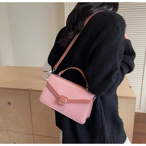 Detail of pink crossbody bag with contrasting edges and stylish square buckle on wood table